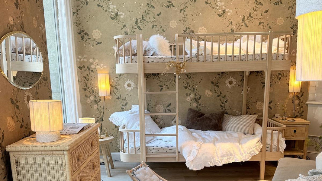Dormitorio infantil con literas de madera Oliver, cómoda de ratán y papel pintado de flores – Nomad Interiors