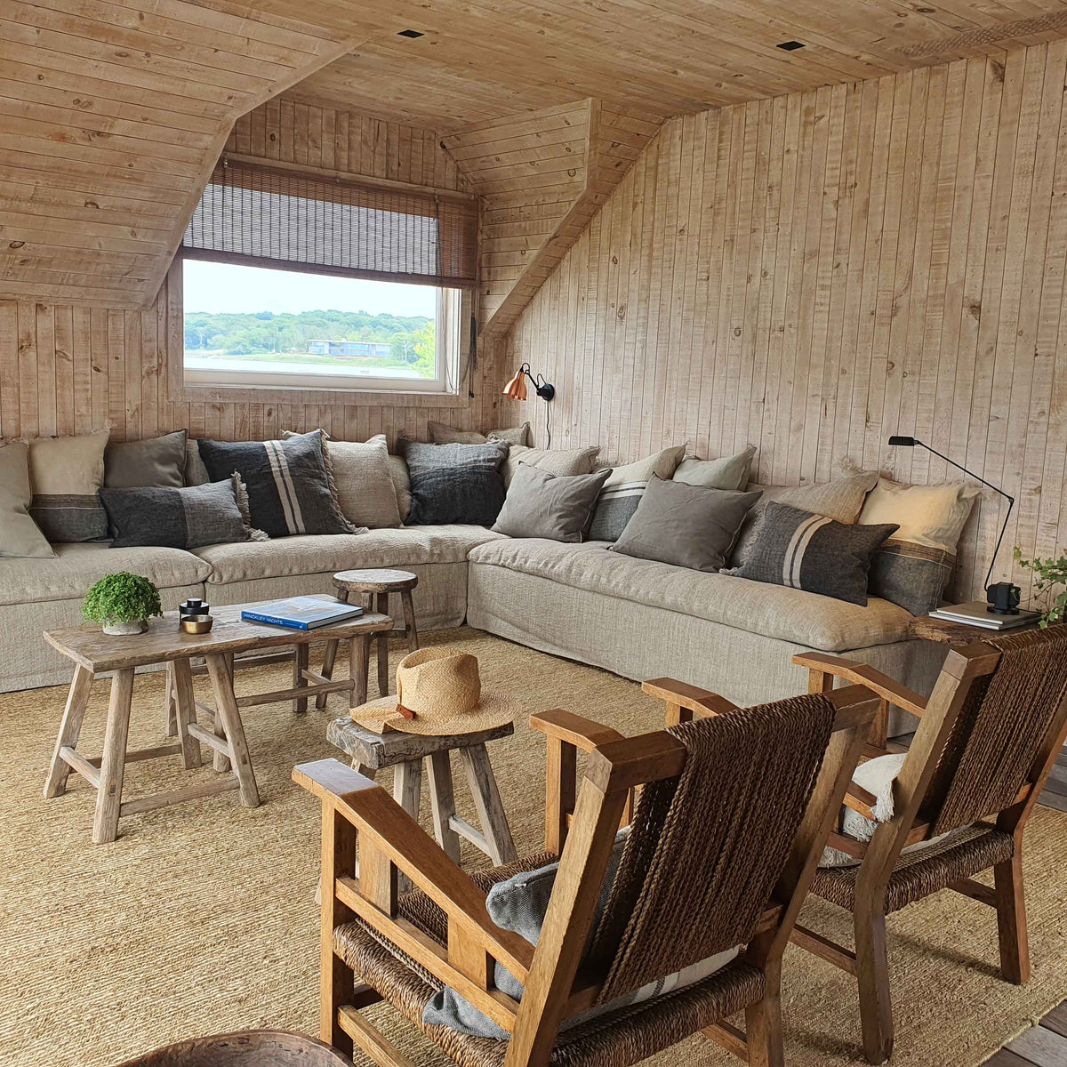 Salón de Hamptons con sofá de lino, revestimiento de madera y butacas de fibras naturales